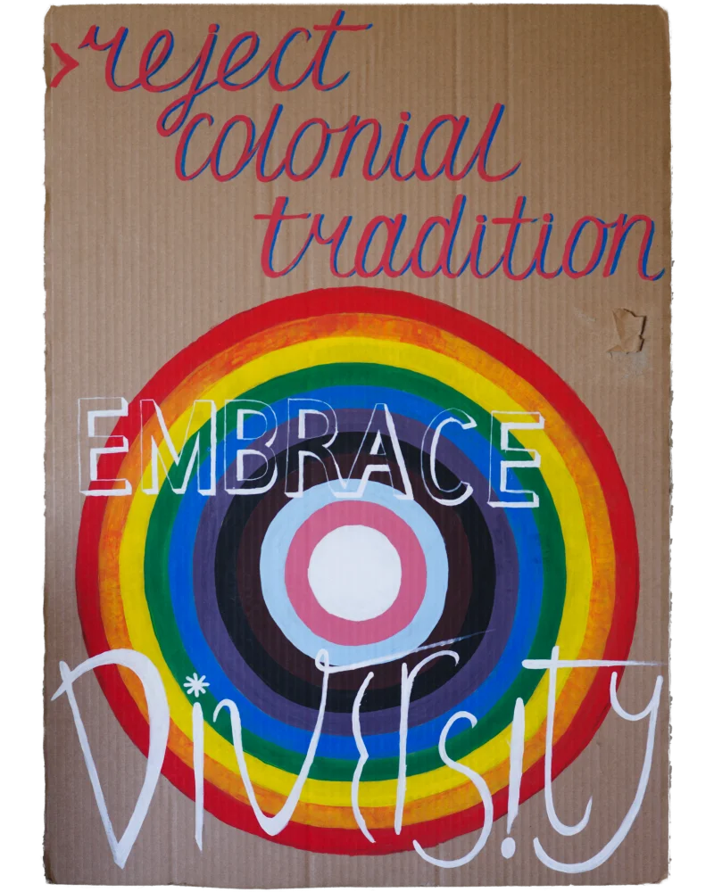 Reject colonial tradition embrace diversity inscription with the colors of the Progress Pride flag on the background